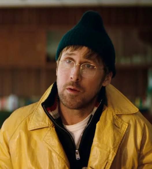 Foto de Ryland Grace, interpretado por Ryan Gosling, no filme Project Hail Mary. Ele é um homem branco, de touca escura que se projeta pro topo como uma gota. Usa óculos, sueter e uma jaqueta de couro amarela