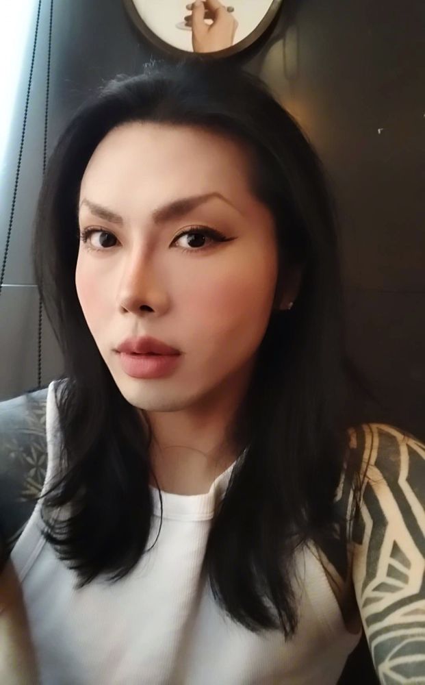 A picture of Mishima Kitan wearing a white tank top. They are in a restaurant. 

Note: This picture is processed through ArtShield for anti-AI measure.