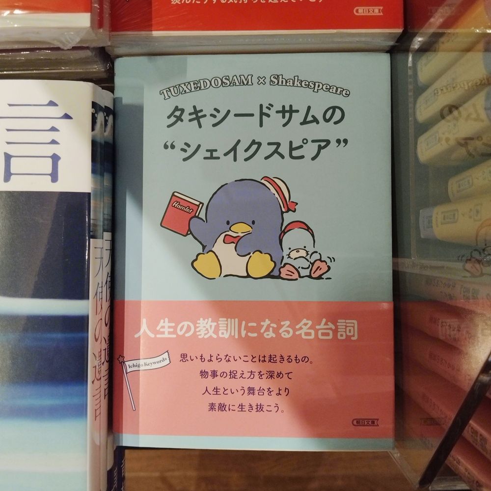 A picture of the Japanese book "Tuxedosam No Shakespeare". There is an illustraion of Tuxedosam (a penguin character from Sanrio) with his seal friend, Chip. Tuxedoasm is holding a pink book with the title, "Hamlet".