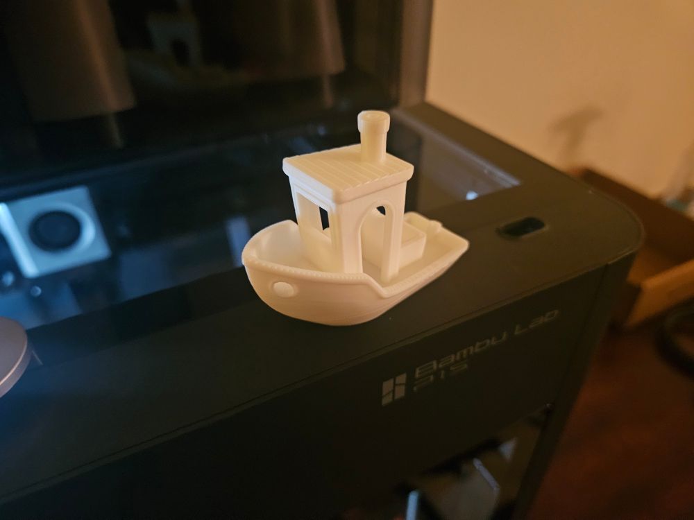 Close-up photo of a 3D printer with a small white model of a boat on top of it