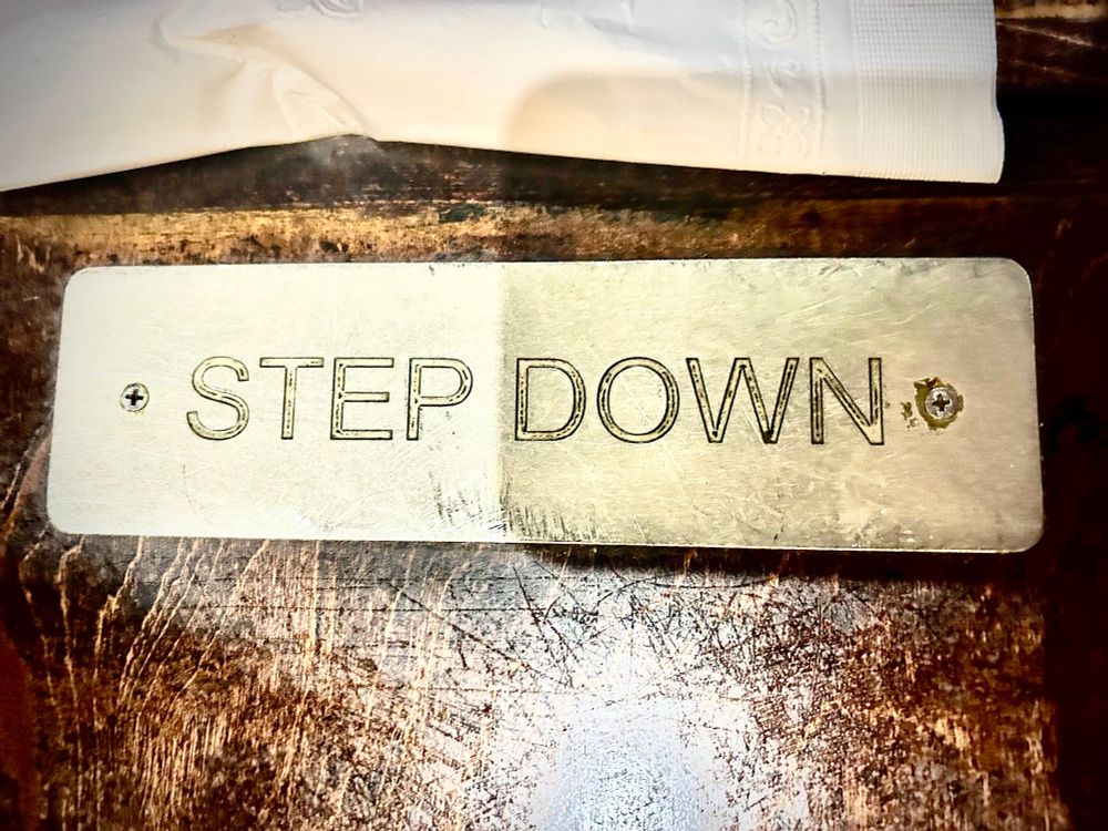 Small metal sign screwed on to table saying “STEP DOWN.”