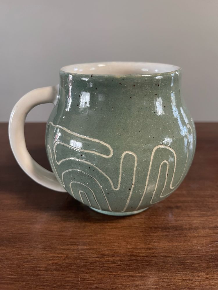 a greenish blue mug with a white handle. there are maze like lines twisting around the bottom half of the mug. 