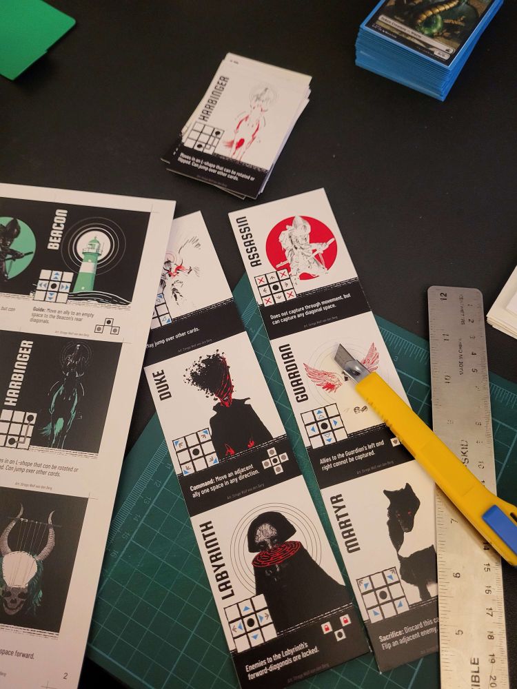 Some Crownfell cards printed on card stock, in the process of being cut with a knife and ruler. 