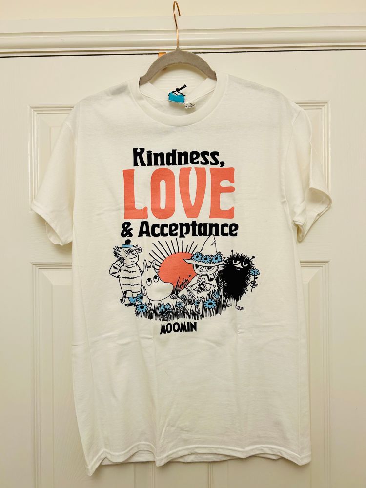 A photo of a white t shirt hanging on a door. The t shirt features characters from the Moomins and is printed with the words “Kindness, love & acceptance”.