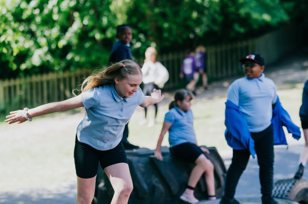 A photo of children in the playground at school. They are wearing blue polo shirts and black trousers or shorts.