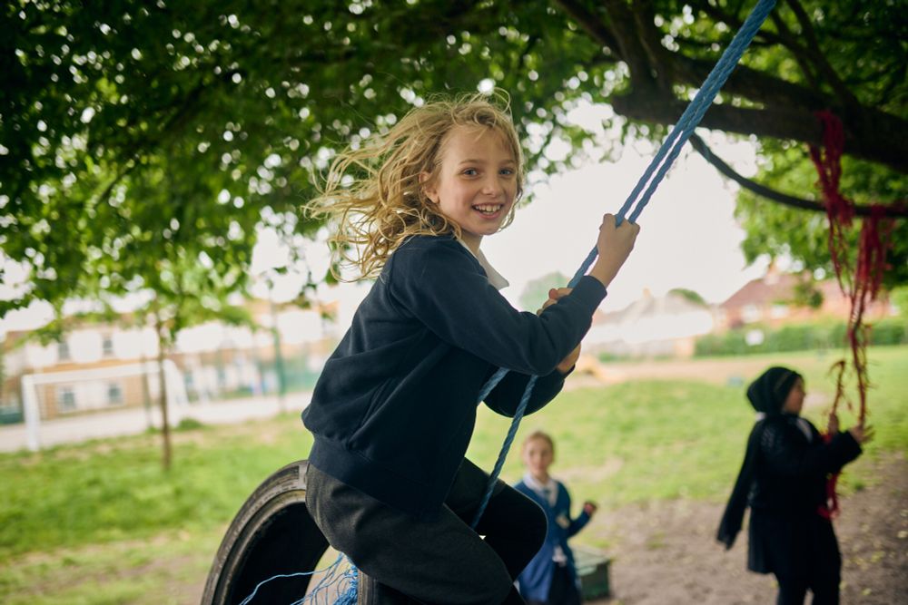 A child swinging on a rope and tyre swing in a school playground. They are smiling and looking at the camera.
