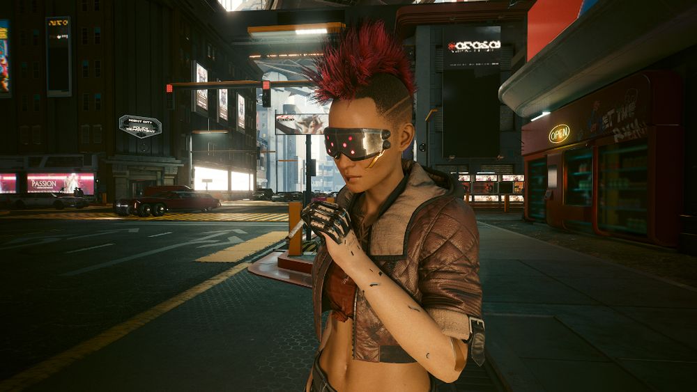 Screenshot of the game Cyberpunk 2077 featuring my version of the protagonist V - a heavily augmented human woman wearing a cropped bomber jacket, with a pink mohawk and tech goggles with mutli-faceted pink lenses over her eyes. She's smoking.