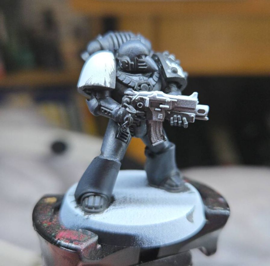 Photo of a single Games Workshop Space Marine miniature in the midst of being painted, held on a painting handle.