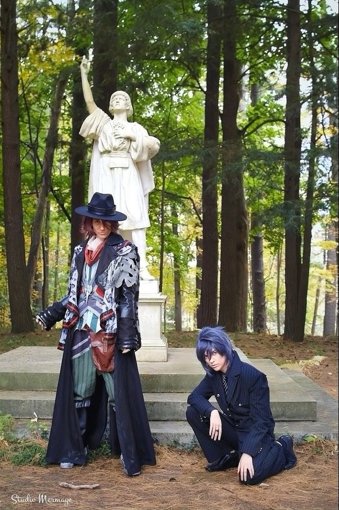 cosplayers of Ardyn and Noctis from FFXV, in front of a marble statue reaching towards the sky. 