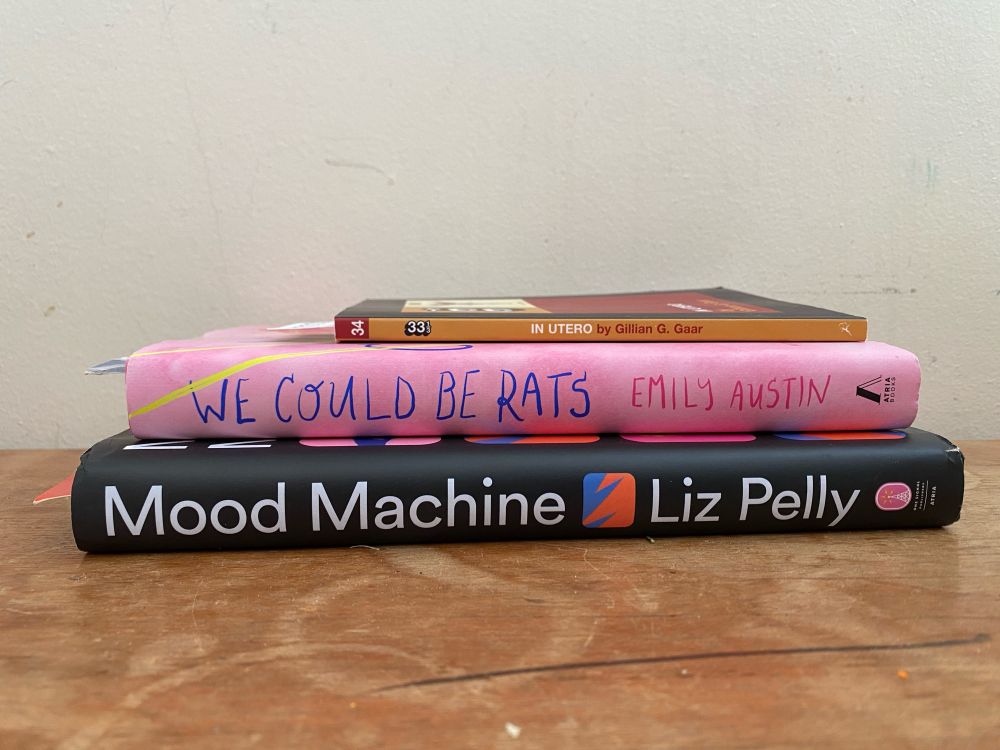 A stack of three books, organized by size (smallest on top to largest on bottom), viewed from the side so that the spines can be seen. 

The top book is the 33 1/3 book on “In Utero” by Nirvana, written by Gillian G. Garr. 

The middle book is “We Could Be Rats,” written by Emily Austin. 

The bottom book is “Mood Machine: The Rise of Spotify and the Costs of the Perfect Playlist” written by Liz Pelly