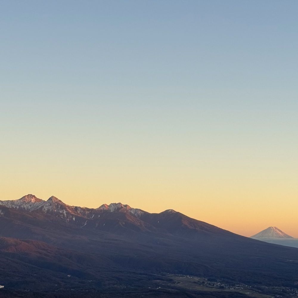 ビーナスラインから撮影した秋の早朝、左に八ヶ岳連峰、右に富士山を望む。朝焼けに染まる空と山々のシルエットが織りなす長野県の山岳風景。
-A mountain vista captured from Venus Line in early autumn morning. The silhouettes of Mount Yatsugatake range on the left and Mount Fuji on the right stand against the dawn-painted sky in Nagano Prefecture.-