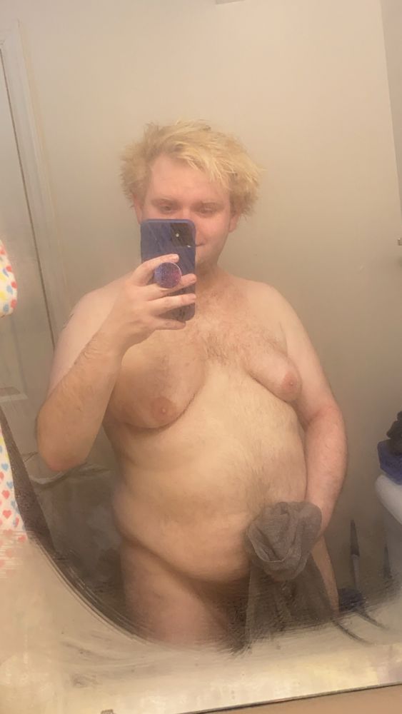 A heavy-set blond man takes a post-shower selfie, nude but covering his crotch with a towel