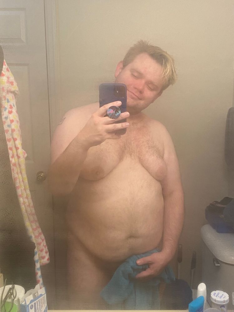 A mirror selfie after a shower. I am naked but holding a towel in front of my crotch.