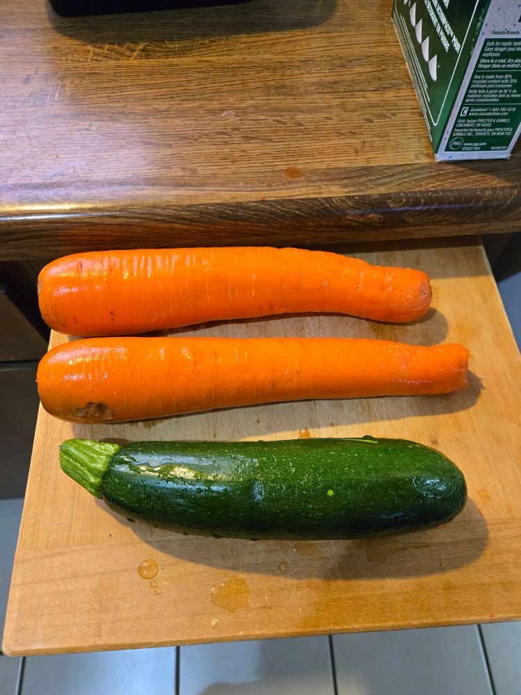Two carrots and a zucchini on a cutting board. The carrots are larger than the zucchini. 