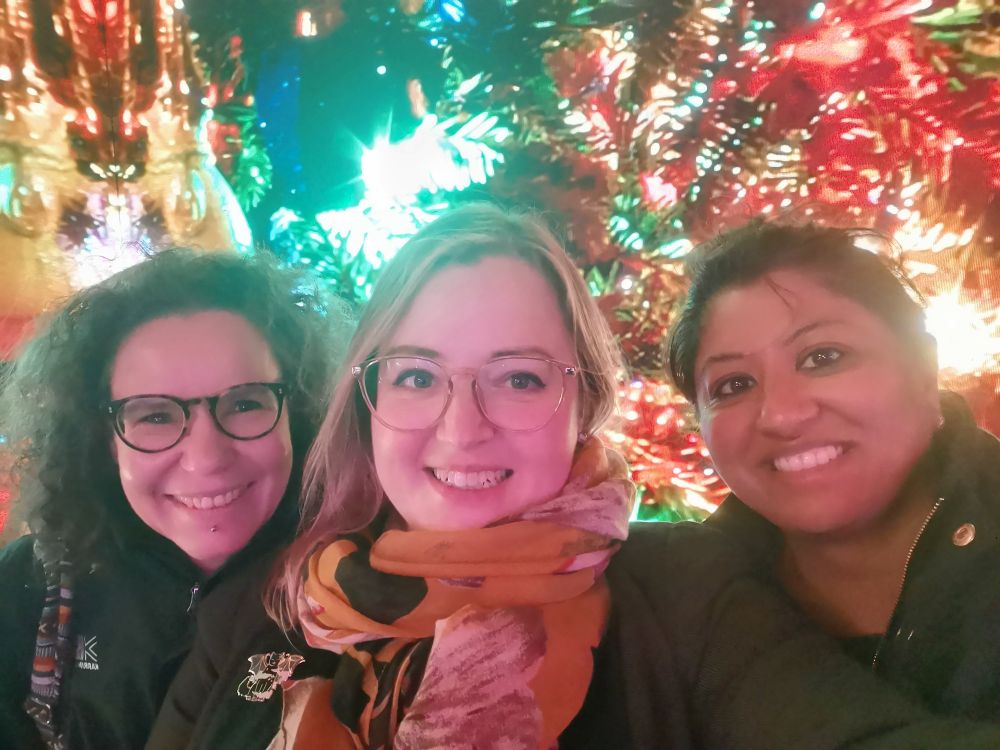 Gi Helfer, Rebecca Dumbell and Preeti Jethwa smiling in front of a Christmas tree