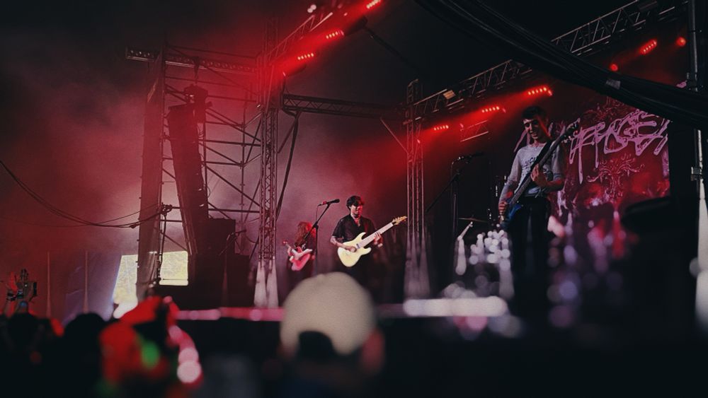 Unprocessed on the Dogtooth stage at Download Festival. Photo of three people playing guitars. The stage is lit in red and a large tapestry featuring the band’s logo hangs in the background.