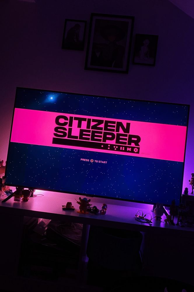A tv screen showing the Citizen Sleeper loading screen with pink and purple backlighting 