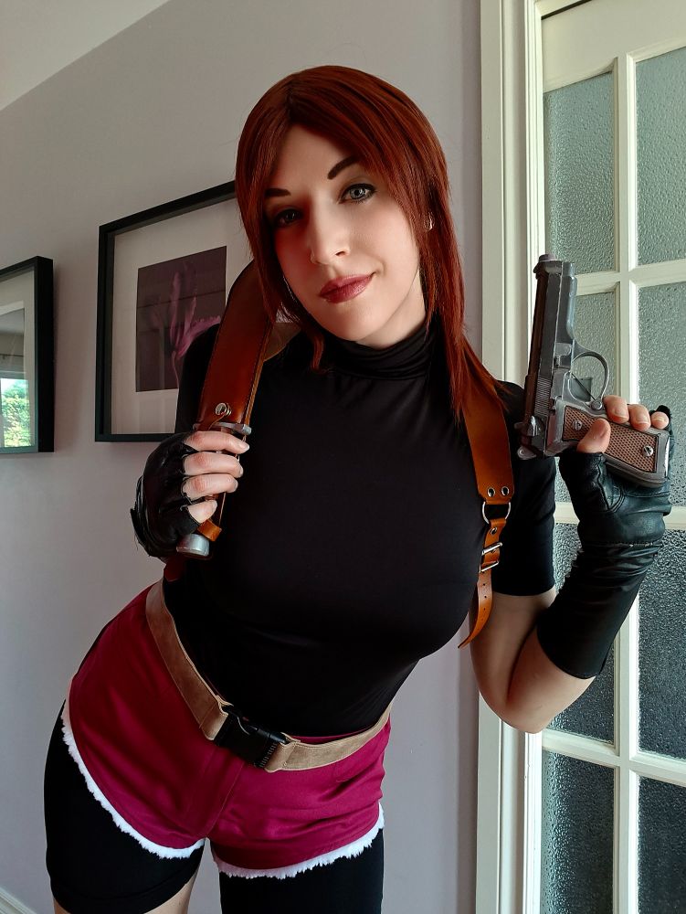 Sheenah is cosplaying as Claire Redfield from the video game Resident Evil 2 (1998). She took off her red vest and is holding a fake gun.