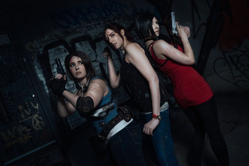 Valky, Sheenah and LZ are cosplaying as Jill Valentine, Claire Redfield and Ada Wong respectively. They're all holding fake weapons and their clothes and body are dirty and smeared with fake blood.