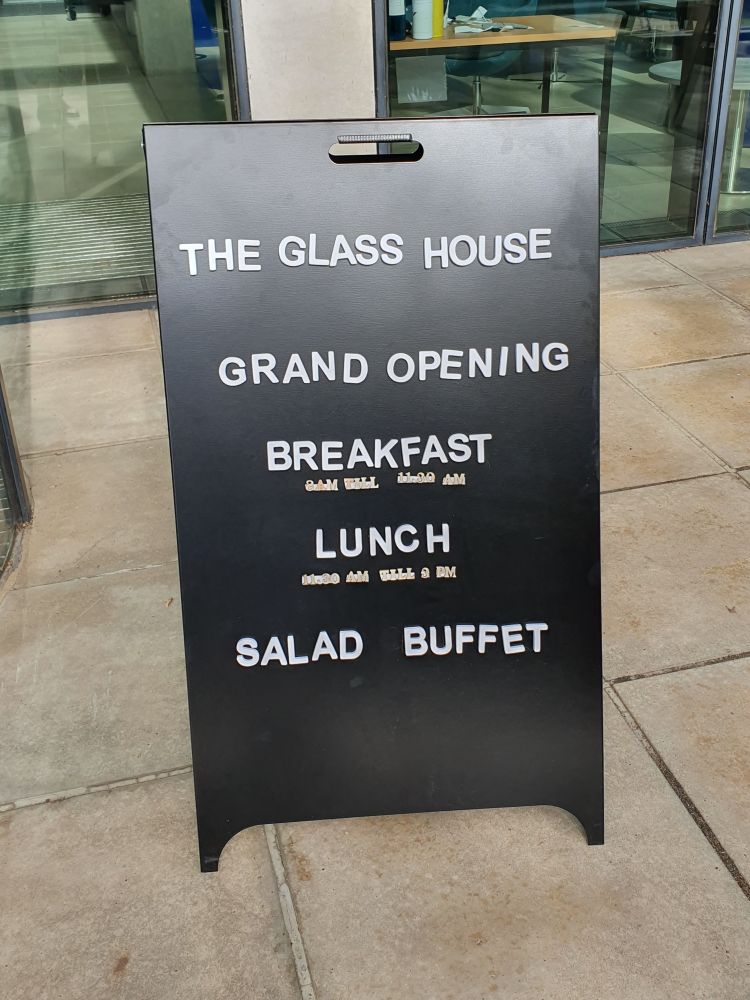 A board outside the front of the Manor Road building which says 'The Glass House, Grand Opening, Breakfast, Lunch, Salad Buffet.'