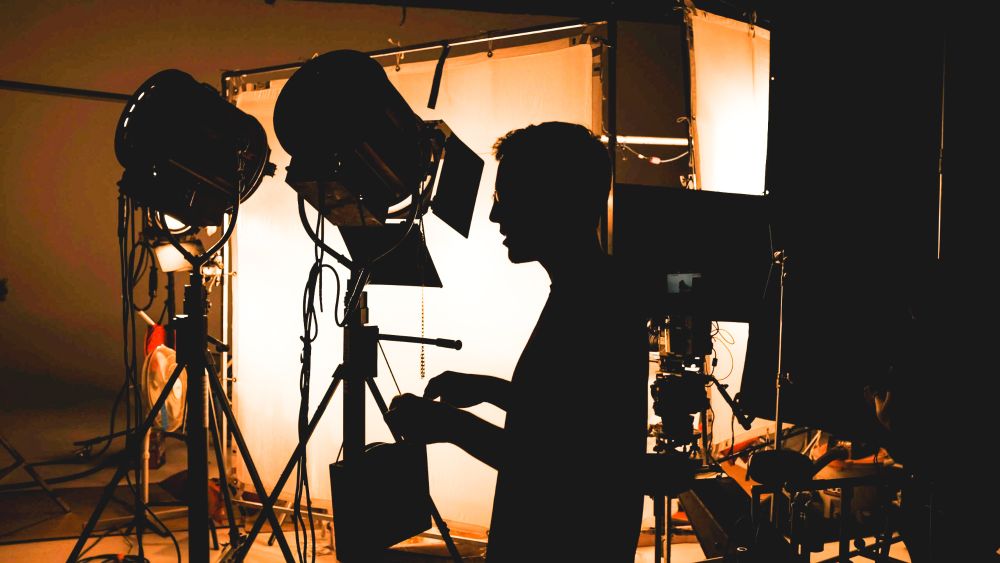Cinema Lights and 12x12 scrims fill the background while a crew member walks in front of the structure, silhouetted by the bright light in an otherwise dark space. 
