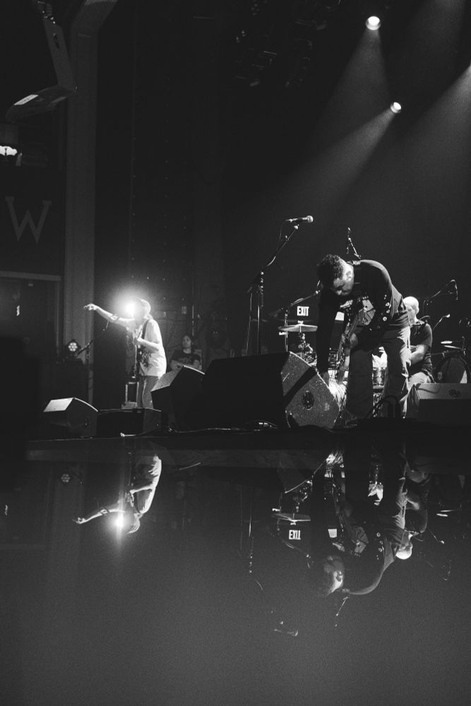 Post-hardcore band, Quicksand performs on stage. A specialty lens filter produces a mirroring effect of the band on stage. Picture is in black and white 