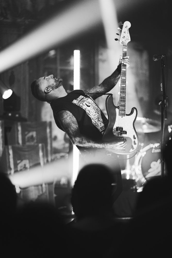 Black and white - The bass player of bayside lifts his bass upright while performing on stage