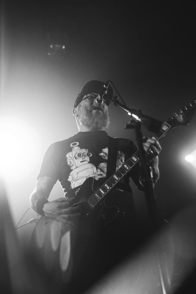 Black and white- The singer of the Smoking Popes plays guitar and sings. Bright lights envelop behind him