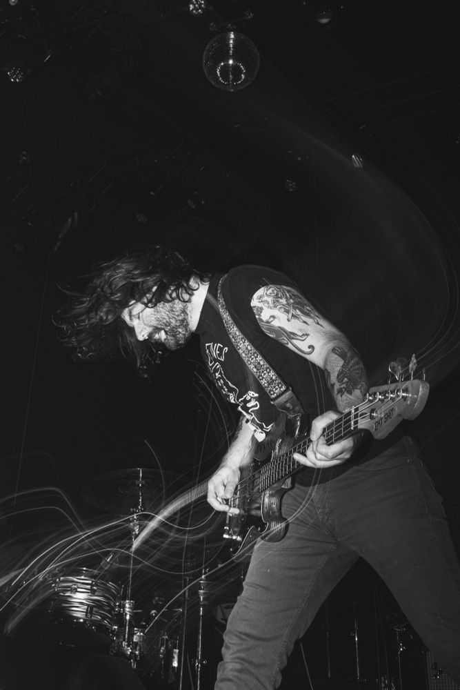 The bassist of the band, HELP playing intensely during a recent concert. Image is monochrome
