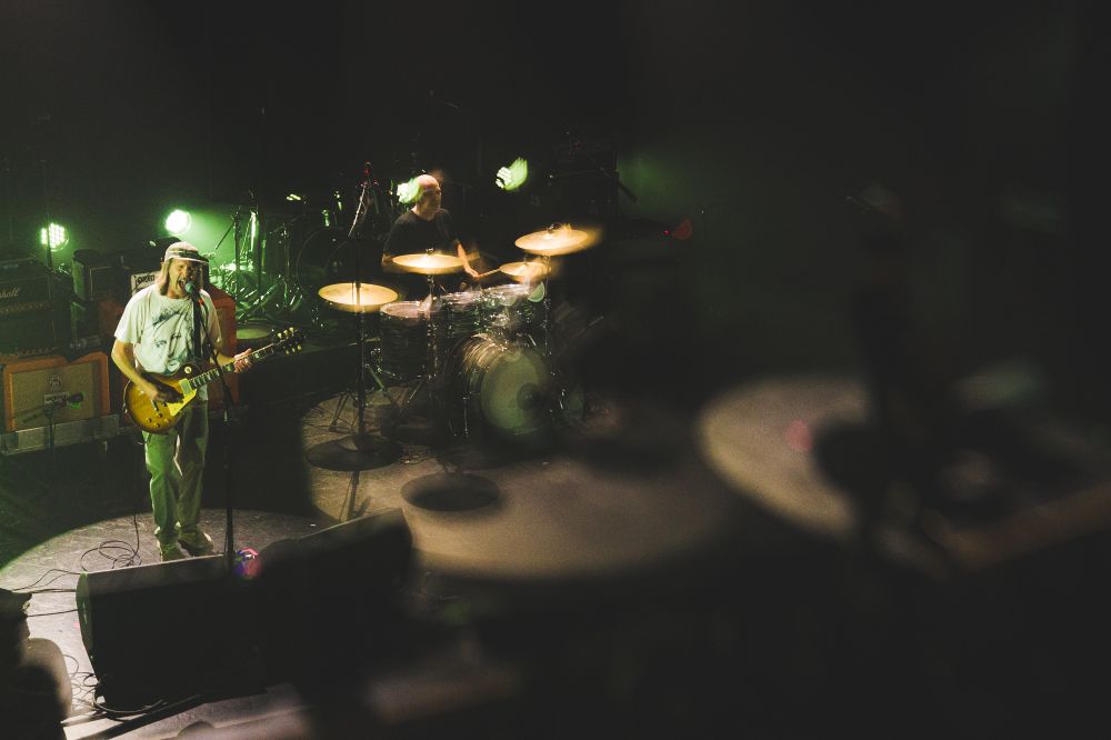 Post-hardcore band, Quicksand performs on stage. Picture taken from a balcony level, overlooking the stage. The guitarist is featured and is brightly lit, while a lens distortion effect obscures the rest of the stage 