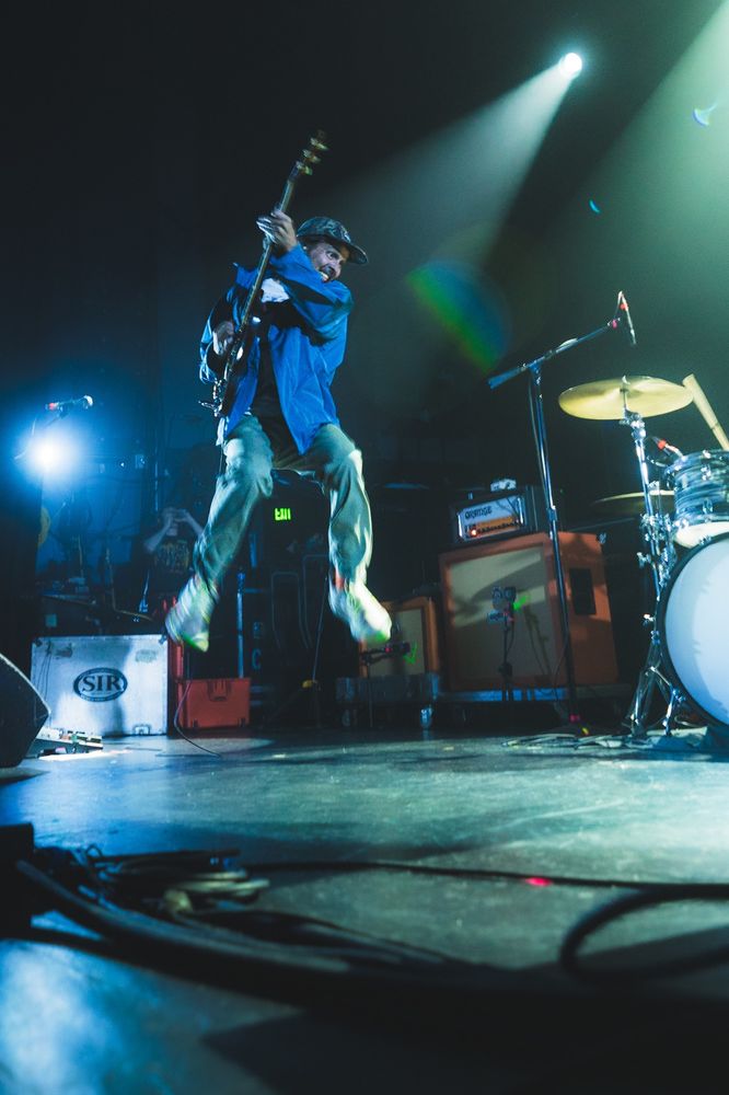Guitarist of the band, Quicksilver, jumping with his guitar during a performance. The stage stretches in the foreground to the airborn guitarist. 