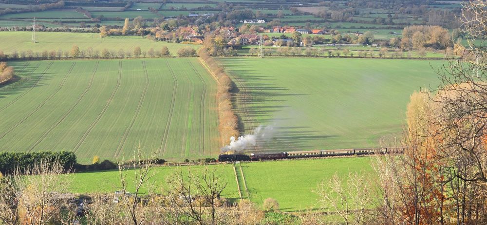A steam engine ( USATV S160 from the 
Baldwin Locomotive Works, Philadelphia, USA, built in 1945) pulls her carriages across a sundrenched autumnal landscape