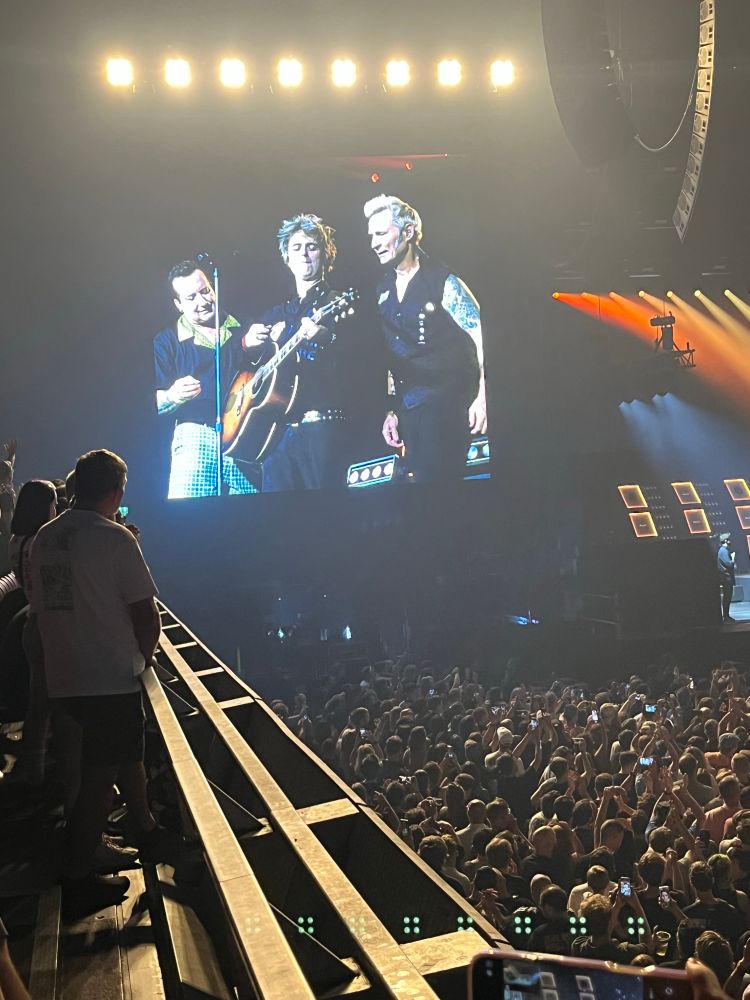 Tré Cool, Billie Joe Armstrong, and Mike Dirnt standing side by side at the end of a Green Day concert. Billie is holding a russet coloured guitar. They just finished “Good Riddance (Time of your Life)” 