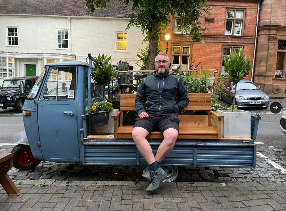 Man sitting on a vintage italian truck which has a parklet and lots of flowers in it