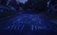 In a residential suburb, a street has the message "there is still time" written in chalk on the road. This scene is from the movie "I Saw the TV Glow."