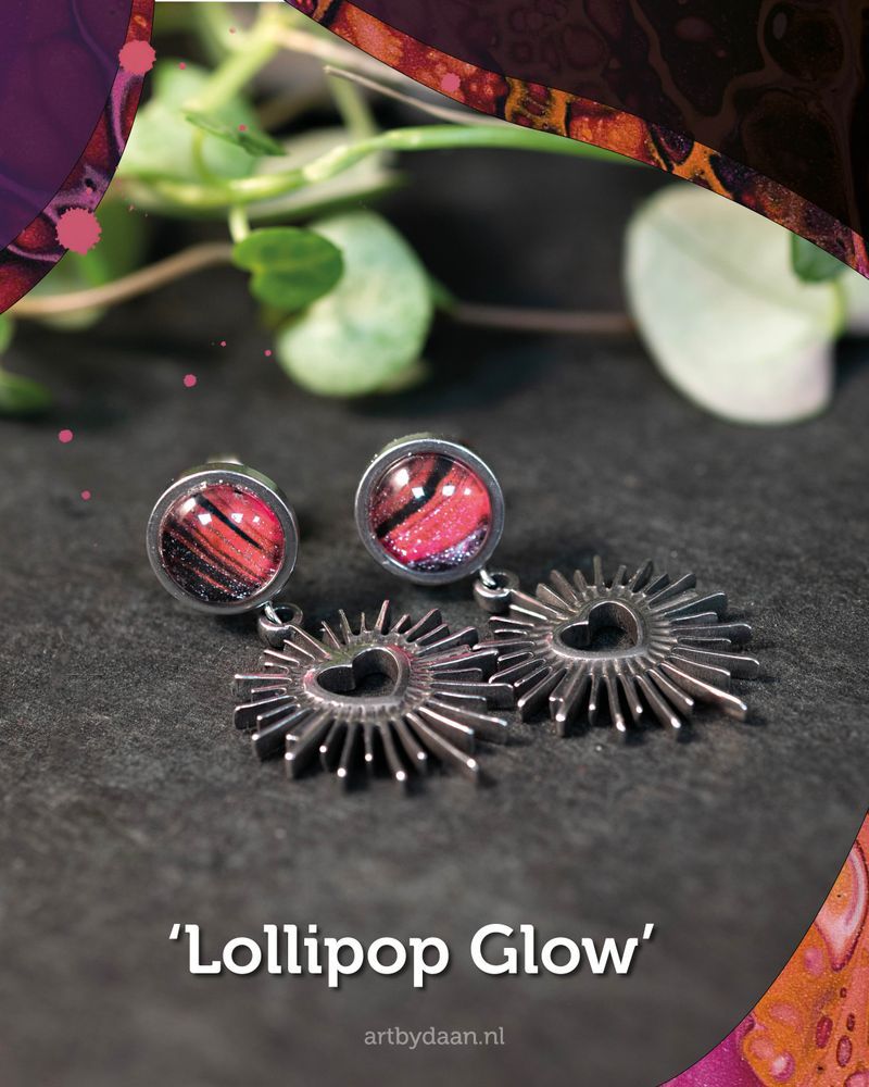 Close-up van de oorbellen ‘Lollipop Glow’: donkerroze handgeschilderde stenen met een zilverkleurige hartjeshanger, speels en modern.
\
