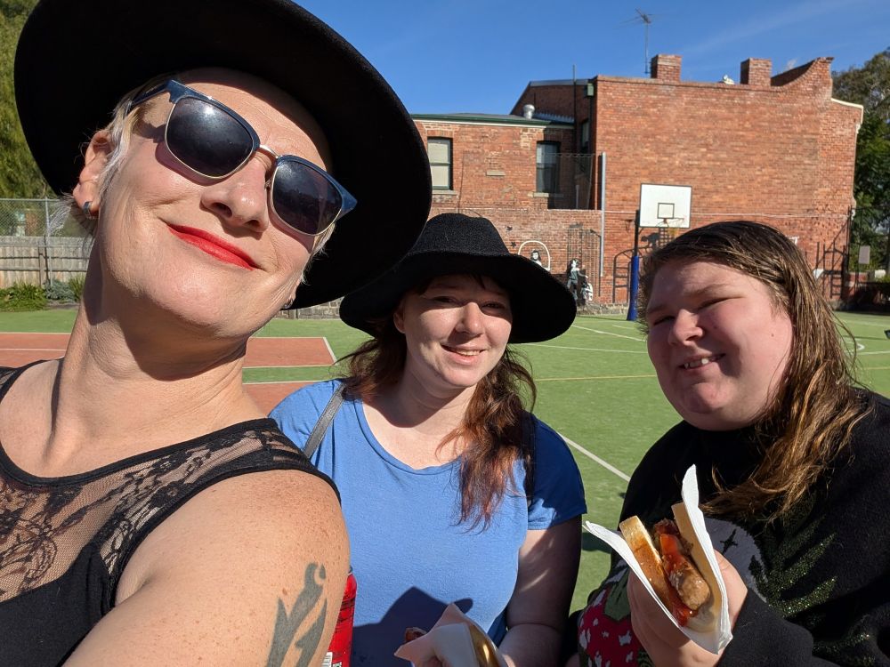 Three people smiling at the camera and holding sausages in bread cos they're voting in Australia and that's the thing you do