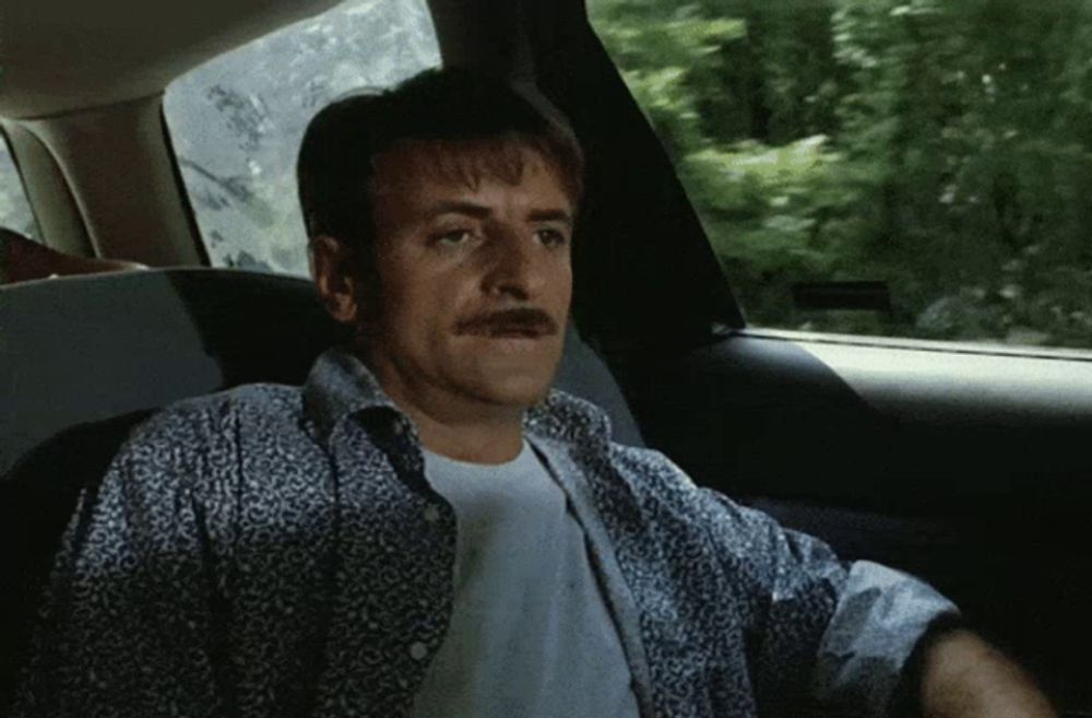 a man with a mustache sitting in the back seat of a car