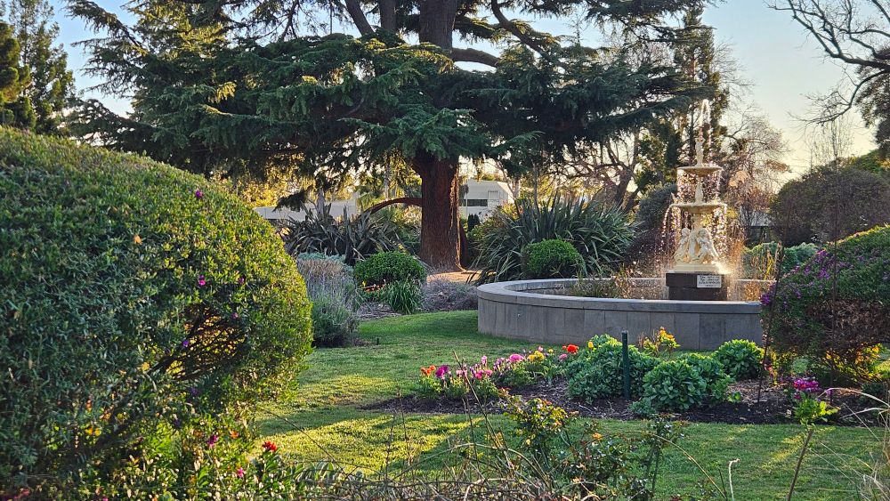A park garden in early morning light. The fountain is white and the kind supported by statuettes