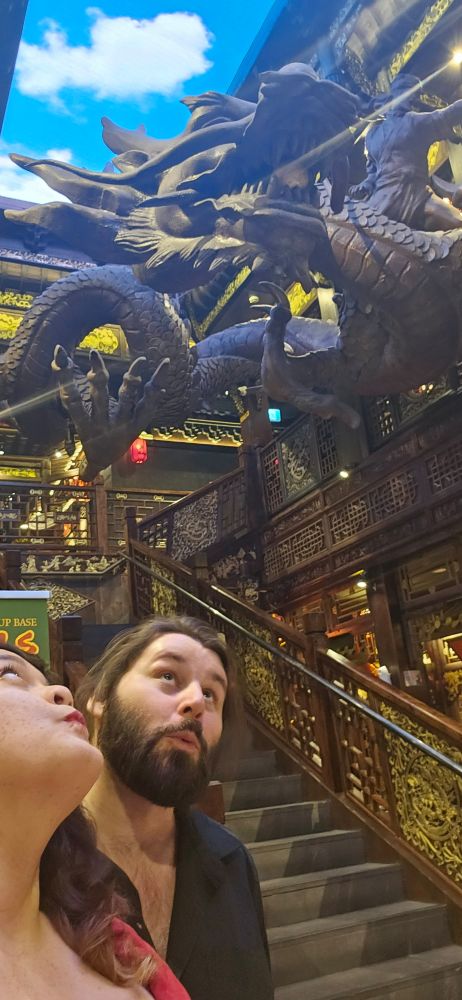 A couple looks up to a floating dragon statue in the middle of a restaurant 