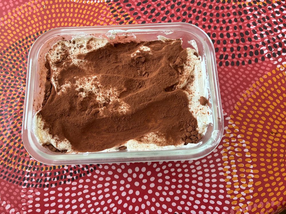 Photo d’un tiramisu vus de haut. Il est dans un petit plat rectangulaire, et on y voit la crème et le cacao. 