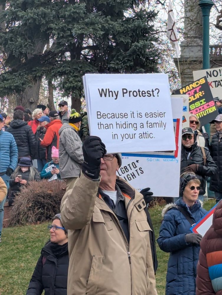 A man holding a sign that says: "Why Protest? Because it is easier than hiding a family in your attic"