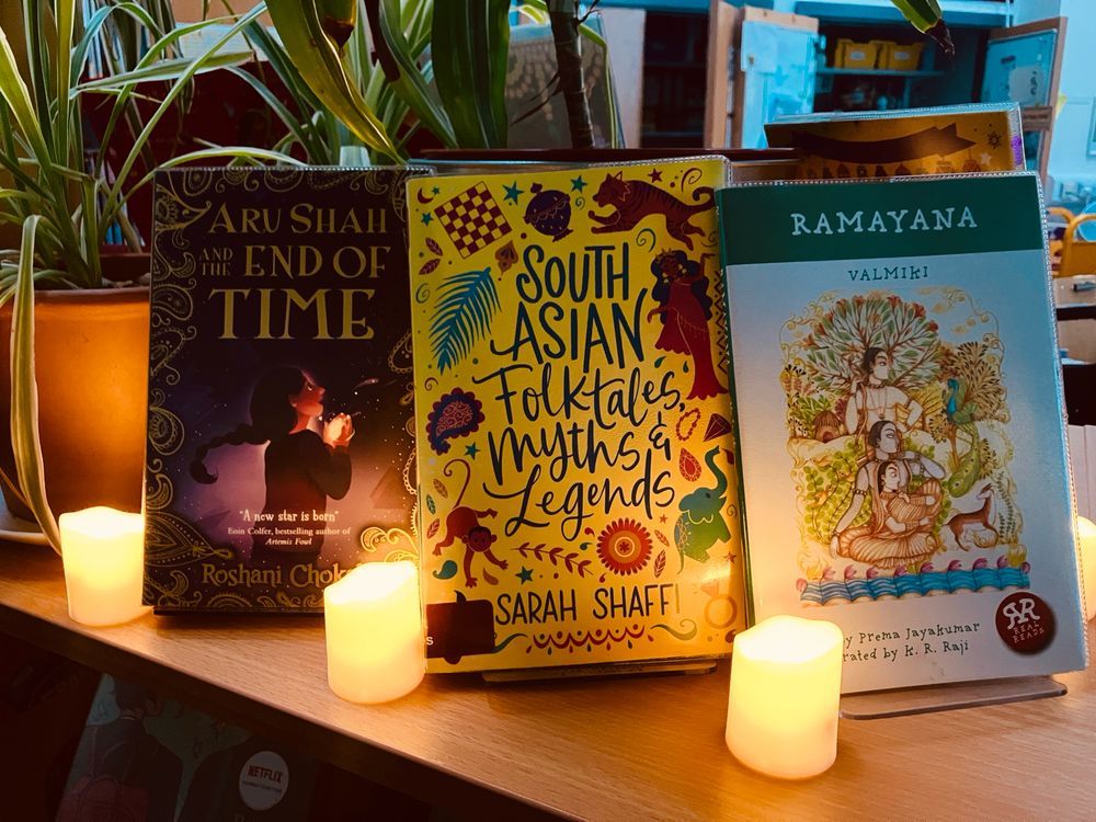 More books on display including a version of the Ramayana and a collection of South Asian folk tales and myths. In front of the books are small LED candles. 