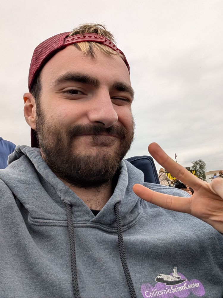 Me in a backwards maroon hat. Wearing a hoodie. Throwing up a peace sign and winking