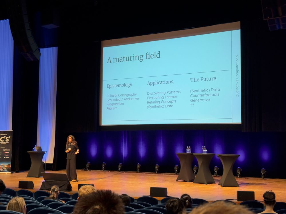 Laura Nelson on stage presenting her keynote at IC2S2. The slide lays out "A maturing field" of Computational Qualitative Research