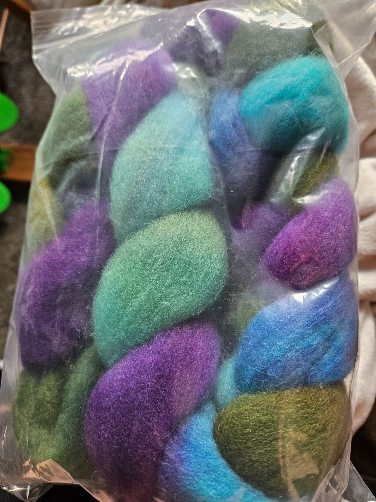 Wool roving in a ziplocked bag. It is dyed the colorway "dragonfly" which is a mix of purple, blue and green. 