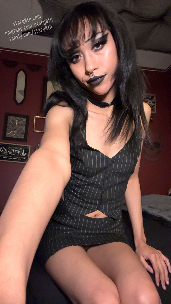 Star sitting on bed looking at the camera wearing a pinstriped vest and matching skirt 