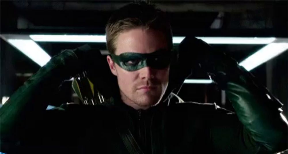 a man wearing a green mask and gloves is sitting in a dark room .