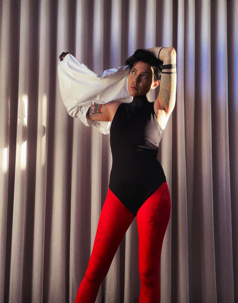 full body pic of me dressed as tyler in red stockings + leotard combo pulling shirt over head in slightly dif pose w a leg to the side 