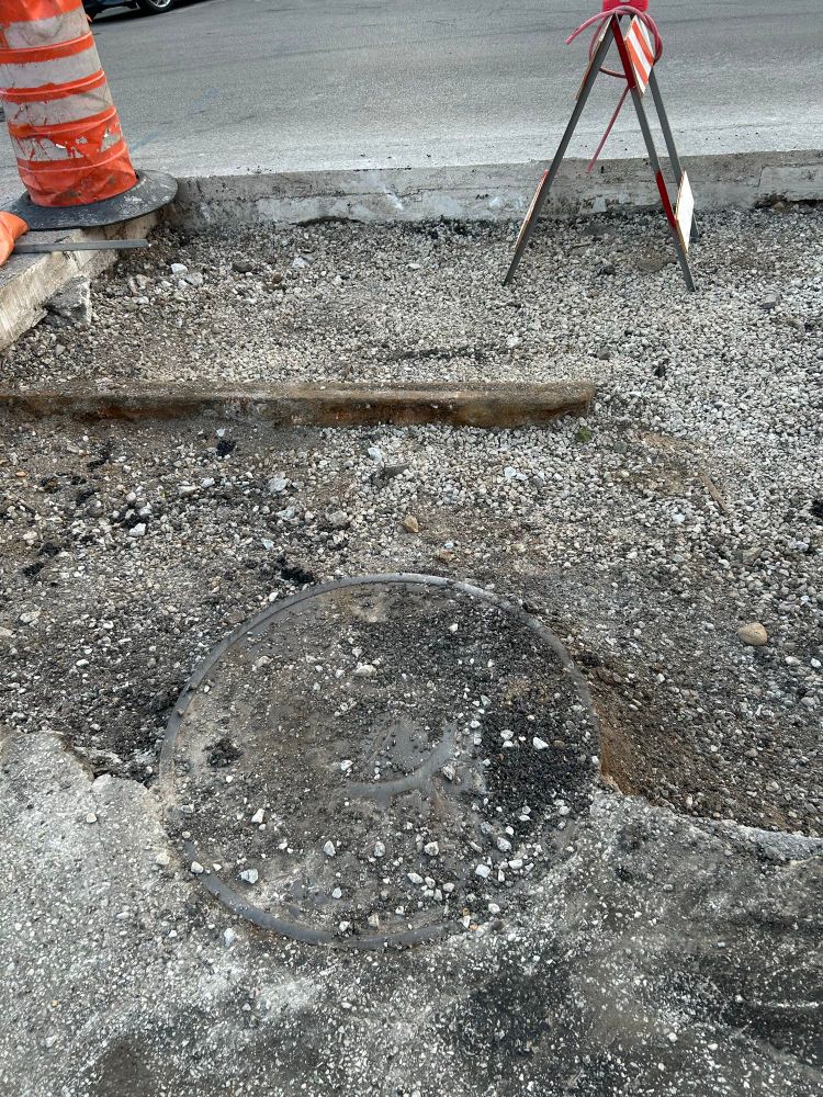 Part of street cut out, very abused manhole cover, with an old streetcar track in background. 